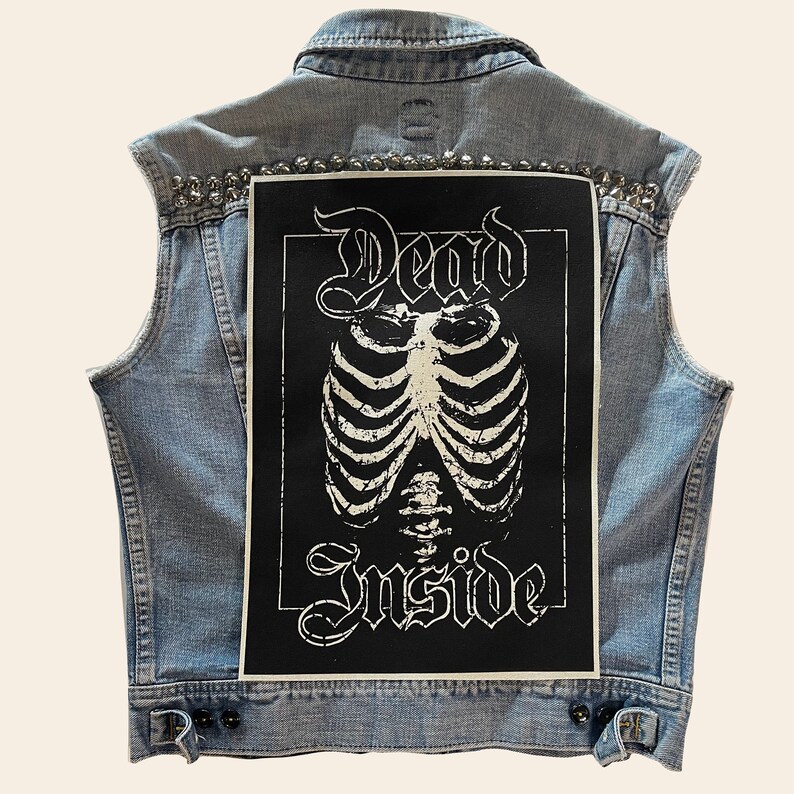 May include: A light blue denim vest with silver studs and a black patch on the back. The patch features a white skeleton ribcage with the words "Dead Inside" in a gothic font.