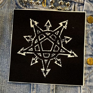 Puede incluir: Parche termoadhesivo negro y blanco con un dise&ntilde;o de estrella blanca. La estrella tiene un pentagrama en el centro y est&aacute; rodeada de 12 puntas.