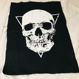 Op de afbeelding: Een zwarte stoffen patch met een wit schedelontwerp. De schedel heeft een driehoekige vorm eromheen en drie lijnen over de ogen.