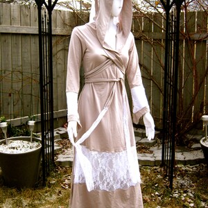 May include: A long, beige hooded dress with a white lace trim. The dress has a wrap-style bodice and a flowing skirt.