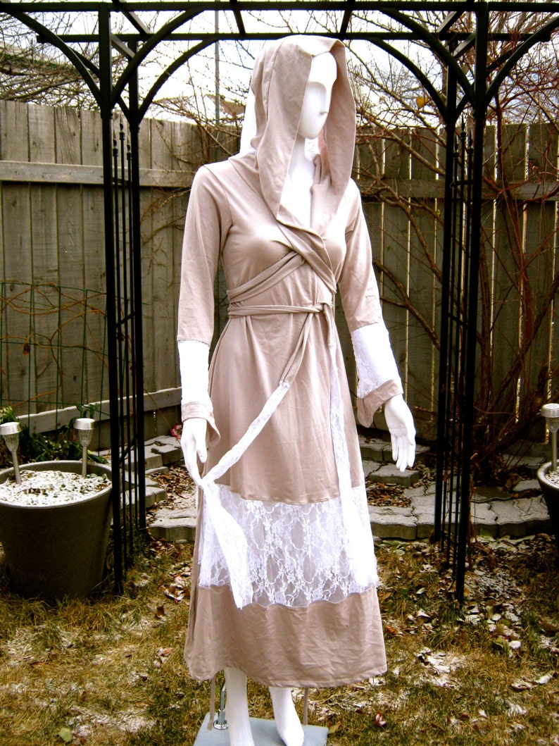 May include: A long, beige hooded dress with a white lace trim. The dress has a wrap-style bodice and a flowing skirt.