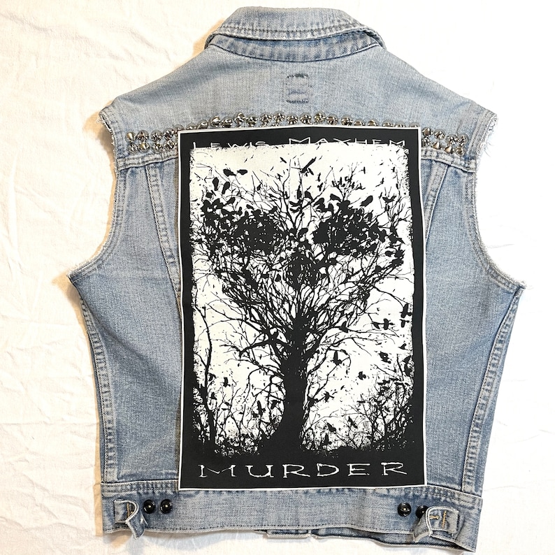 K&ouml;nnte beinhalten: Eine hellblaue Jeansweste mit einem schwarzen und wei&szlig;en Patch auf der R&uuml;ckseite. Der Patch zeigt einen Baum mit V&ouml;geln und den Text "Lewis Mayhem Murder".