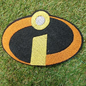 May include: An embroidered patch featuring an oval shape with an orange border, a black center, and a yellow letter i with a white dot above it. The design is stitched with dense thread, creating a textured surface with clear, defined edges.