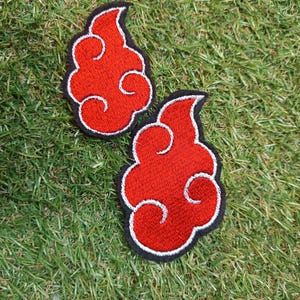 May include: Two embroidered patches featuring a stylized red cloud shape with a white outline and a black border. The cloud design has a swirling, flame-like appearance with rounded edges and a distinct, curved top section on each patch.