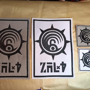 May include: A collection of black and white patches with a circular design featuring a stylized number six and radiating lines. The patches also include the text "ZAL+4" in a bold, angular font. The patches vary in size and are on a neutral background.