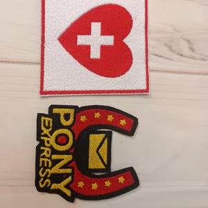 May include: Two embroidered patches. The top patch is a red heart with a white cross on a white square. The bottom patch is a black horseshoe shape with the words "PONY EXPRESS" in yellow and a yellow envelope.