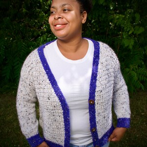 May include: A white and grey cardigan with purple trim and wooden buttons. The cardigan is knitted and has a v-neck.