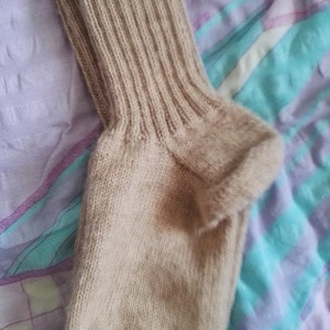 May include: A beige knitted sock with a ribbed cuff. The sock is made of a soft, warm material and is perfect for cold weather.