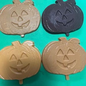 May include: Four pumpkin-shaped items with carved jack-o'-lantern faces. The top left is light tan, the top right is dark brown, the bottom left is medium tan, and the bottom right is a warm golden brown color.