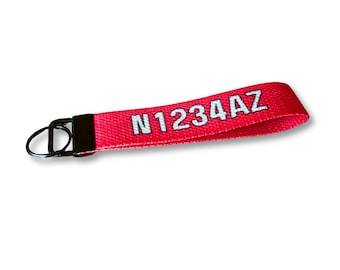May include: A red fabric keychain wristlet with the text "N1234AZ" in white. The keychain has a black metal ring and a black metal clasp.