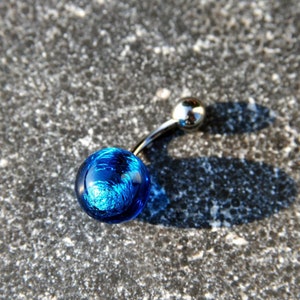Könnte beinhalten: Ein Bauchnabelpiercing aus blauem Glas mit einer silbernen Stange und einer kleinen silbernen Kugel oben.