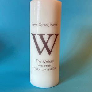May include: White pillar candle with the text "Home Sweet Home" and a large "W" printed on the front. The text "The Westons Ann, Peter. Tommy, Lily and Rose" is printed below the letter.