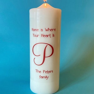 May include: White pillar candle with the text "Home is Where Your Heart Is" and the letter "P" in a cursive font. The text "The Peters family" is also printed on the candle.