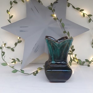 May include: A green and black ceramic vase with a star-shaped metal ornament and a string of lights with green leaves.