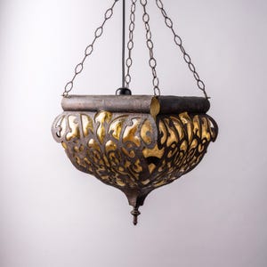 Puede incluir: Lámpara colgante ornamentada, con un marco de metal oscuro envejecido y un diseño de filigrana dorada. La lámpara está suspendida por cadenas y presenta una parte inferior decorativa y puntiaguda. El diseño recuerda a la iluminación vintage o antigua.