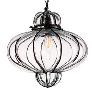 Puede incluir: Lámpara colgante de cristal transparente con forma redondeada y decorativa, con detalles en metal negro. La lámpara tiene una bombilla de estilo vintage y está suspendida de un cable negro. El diseño recuerda a una linterna.