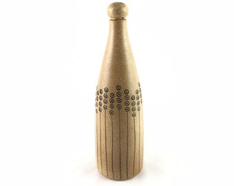 May include: A tan ceramic bottle with a round top and a black geometric design. The bottle has a textured surface.
