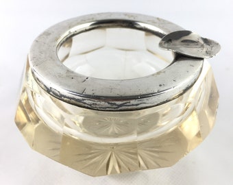 May include: A clear glass ashtray with a silver rim and a silver lid. The ashtray has a cut glass design.