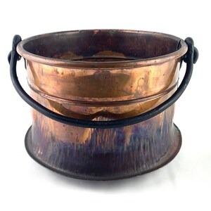 May include: A copper bucket with a black metal handle. The bucket has a hammered finish and a patina.