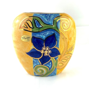 Peut inclure: Un vase en céramique en forme de cœur avec un motif floral. Le vase est peint dans des tons de jaune, bleu, vert et or. Le vase porte une étiquette indiquant "echt vergoldet".