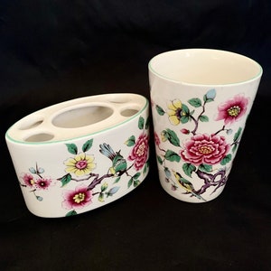 Könnte beinhalten: Ein weißer Keramik-Zahnputzbecher und -halter mit einem Blumendesign mit rosa, gelben und grünen Blumen und Vögeln.
