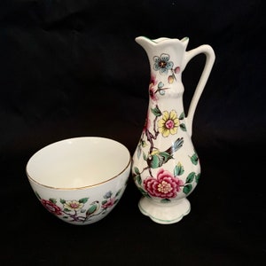 Könnte beinhalten: Eine weiße Porzellan-Kanne und Schüssel mit einem Blumen- und Vogelmotiv. Die Kanne hat ein grünes, gelbes, rosa und blaues Blumenmuster mit einem grünen Vogel. Die Schüssel hat ein ähnliches Blumenmuster mit einem grünen Vogel.