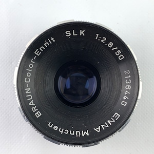 K&ouml;nnte beinhalten: Ein schwarzes und silbernes Kameraobjektiv mit dem Text "ENNA 0 171362", "BRAUN-COLOR-Ennit", "MUNchen", "SLK 1:2.8/50" um den Rand gedruckt.