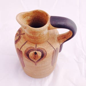 May include: A brown ceramic pitcher with a dark brown handle and a geometric design in brown and white.
