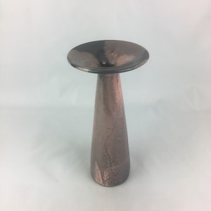 Puede incluir: Un jarrón de cerámica negro y marrón con una abertura ancha y acampanada y una base estrecha y cilíndrica.