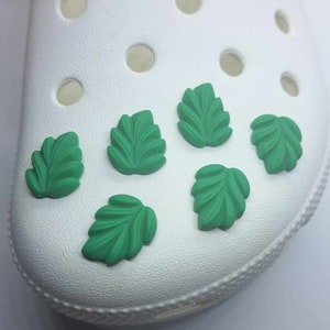 May include: Six green leaf-shaped shoe charms for Crocs or other shoes.