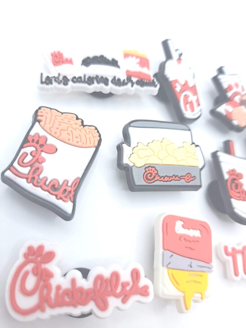 May include: A collection of rubber shoe charms featuring various fast food icons, including a fry container, a drink cup, and a nugget box, all decorated with red and white branding and the Chick-fil-A logo, with one charm displaying the text Lord's calories.