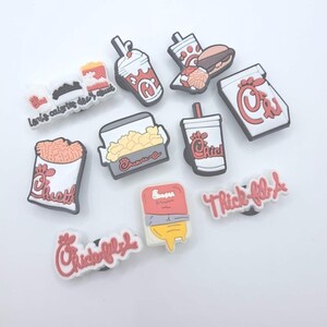 May include: A collection of ten colorful rubber shoe charms featuring fast food icons, including a burger, fries, a milkshake, and a drink cup, along with text-based charms displaying the Chick-fil-A logo and the phrase Lord's calories don't count.