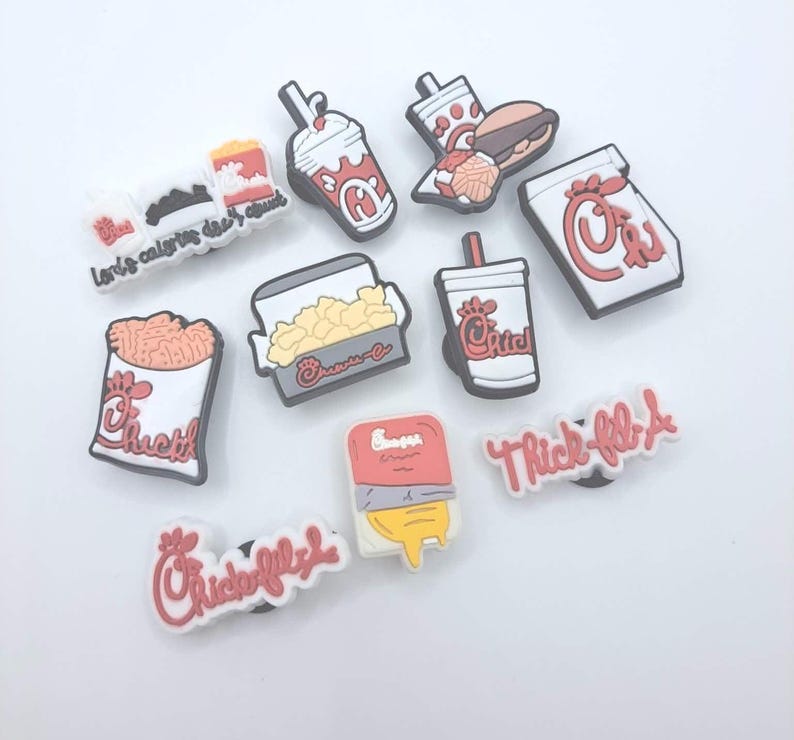 May include: A collection of ten colorful rubber shoe charms featuring fast food icons, including a burger, fries, a milkshake, and a drink cup, along with text-based charms displaying the Chick-fil-A logo and the phrase Lord's calories don't count.