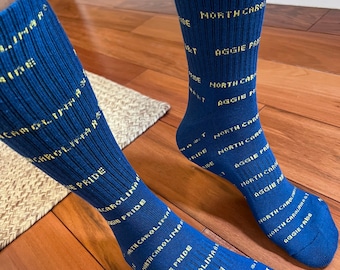 May include: A pair of blue socks with yellow text that reads "North Carolina Aggie Pride".