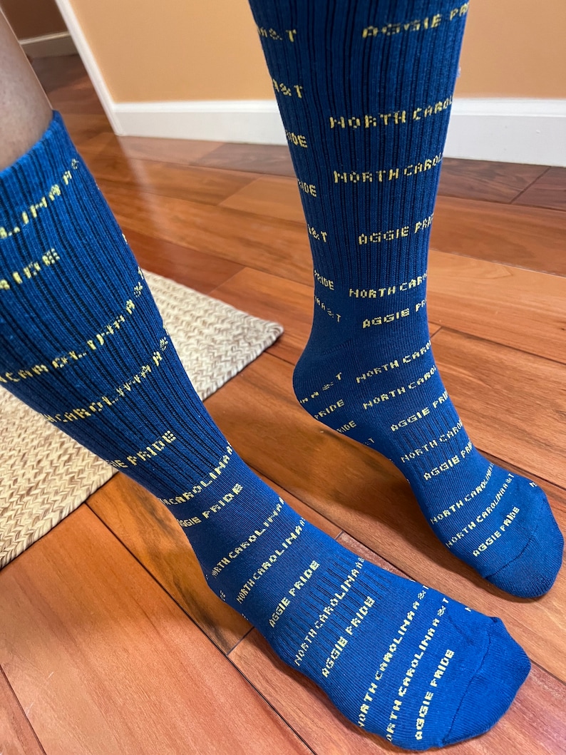 May include: A pair of blue socks with yellow text that reads "North Carolina Aggie Pride".