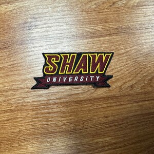 May include: A maroon and gold embroidered patch with the text "SHAW UNIVERSITY" in a banner.