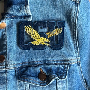 May include: A blue denim jacket with a navy blue and yellow embroidered patch that says "CSU" with a yellow eagle design.
