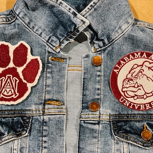 May include: A denim jacket with two patches sewn on. The left patch is a maroon paw print with a white "A&M" in the center. The right patch is a maroon circle with the text "ALABAMA A&M UNIVERSITY" in white and a white bulldog head in the center.