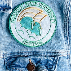 May include: A blue denim jacket with a green and white embroidered patch that says "Norfolk State University Spartans".