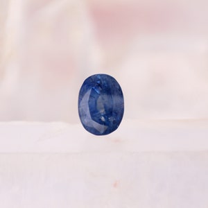 May include: A faceted, oval-shaped sapphire gemstone. The sapphire is a deep, vibrant blue color, with visible internal structures. The gemstone is set against a soft, blurred background, highlighting its color and clarity. The gem is a classic choice for jewelry.
