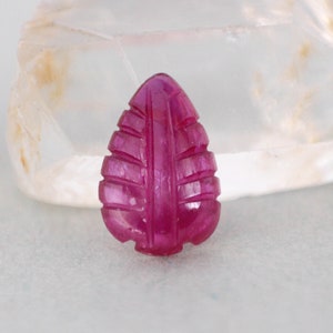 Op de afbeelding: Een gesneden robijn edelsteen in de vorm van een blad. De edelsteen is diep roze van kleur en heeft een gladde, gepolijste afwerking.