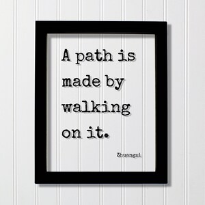 Op de afbeelding: Een rechthoekige zwarte lijst met een witte print met de zwarte tekst in typemachinestijl: A path is made by walking on it. De naam Zhuangzi staat gedrukt in de rechterbenedenhoek van het witte papier binnen de zwarte lijst.
