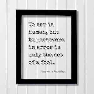 May include: Black and white framed print with a quote by Jean de La Fontaine: "To err is human, but to persevere in error is only the act of a fool."