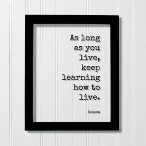May include: A black rectangular frame containing a white print with the black typewriter-style text: As long as you live, keep learning how to live. The name Seneca is printed in the bottom right corner of the white background within the frame.