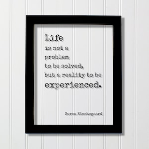 May include: Black framed print with a white background and a quote in black text: "Life is not a problem to be solved, but a reality to be experienced." The quote is attributed to Soren Kierkegaard.