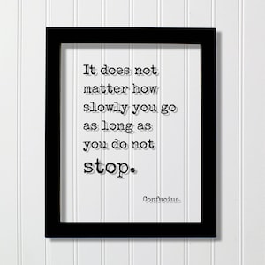 May include: A black rectangular frame containing a white print with the black text: It does not matter how slowly you go as long as you do not stop. Confucius. The lettering is in a typewriter-style font with a subtle drop shadow effect.