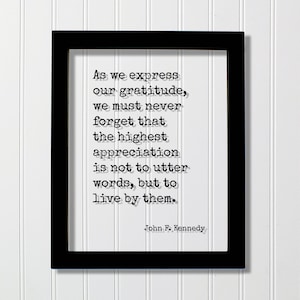May include: Black framed print with a white background and a quote by John F. Kennedy. The quote reads: "As we express our gratitude, we must never forget that the highest appreciation is not to utter words, but to live by them."