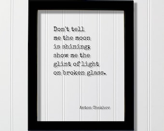 May include: A black rectangular frame containing a white print with the black typewriter-style text: Don't tell me the moon is shining; show me the glint of light on broken glass. The author's name, Anton Chekhov, is printed in the bottom right corner.
