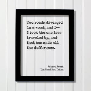 May include: A black rectangular frame containing a white print with black typewriter-style text that reads: Two roads diverged in a wood, and I— I took the one less travelled by, and that has made all the difference. Robert Frost, The Road Not Taken.