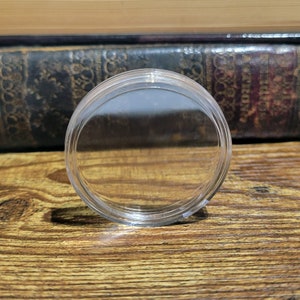 May include: A clear plastic round container with a smooth surface. The container is empty and appears to be made of durable plastic.